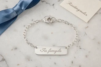 Gourmette en argent pour baptême posée sur marbre blanc avec ruban bleu et certificat, vue de dessus
