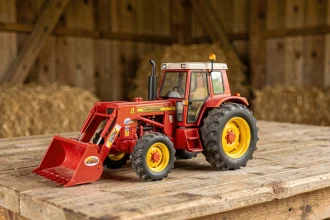 Jouet tracteur agricole rouge et jaune en métal moulé posé sur une table en bois de grange, avec chargeur frontal articulé et pneus en caoutchouc détaillés
