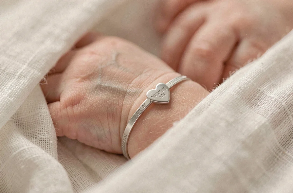 Poignet de nouveau-né avec une gourmette en argent pour baptême sur couverture en lin blanc